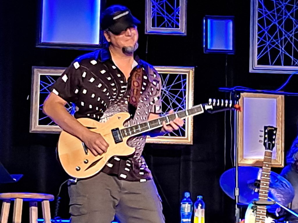 Mike Loce playing electric guitar at a blue-lit concert