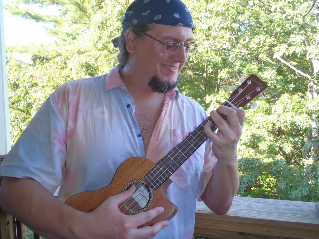 Mike Loce playing a ukulele outside with a blue bandana