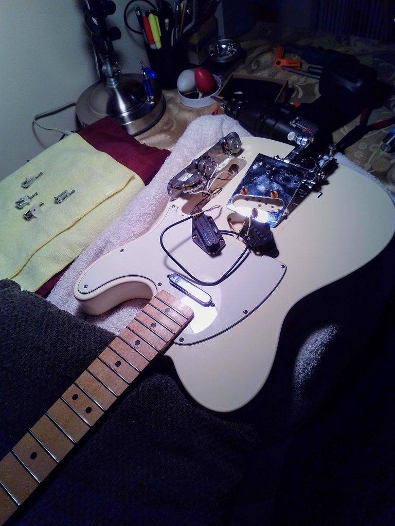 An electric guitar half apart with electronics exposed